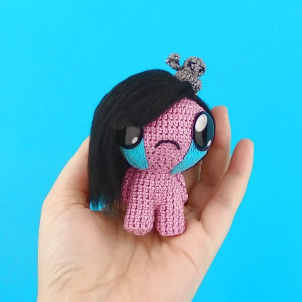 Binding of Isaac Eve Crochet Amigurumi on holding hand over blue background