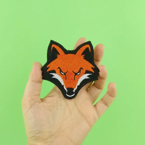 Orange Fox Head Embroidered Patch hold in hand over green background