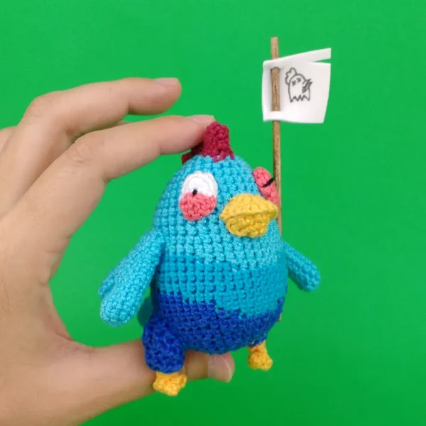 Blue Chicken Crochet Amigurumi holding a flag on holding hand over green background