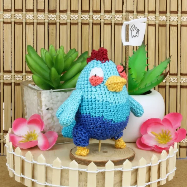 Blue Chicken Crochet Amigurumi holding a flag next to decorative plants and flowers