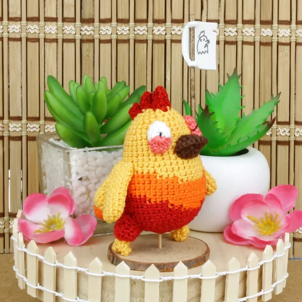 Orange and Blue Chicken Crochet Amigurumi holding a flag next to decorative plants and flowers