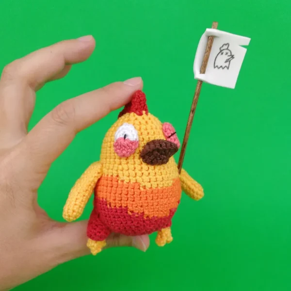 Orange Chicken Crochet Amigurumi holding a flag on holding hand over green background