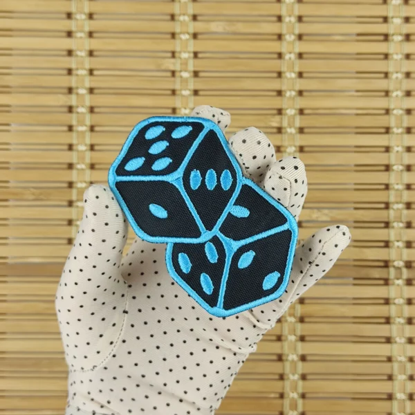 Embroidered patches of a pair of 6-sided dice in neon blue size M in hand