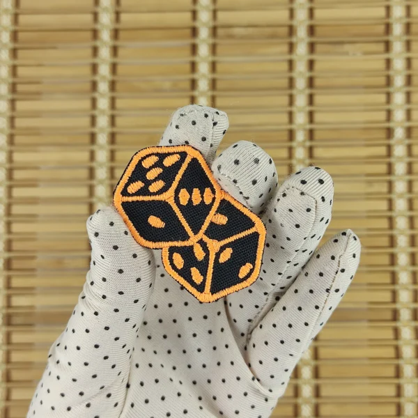 Embroidered patches of a pair of 6-sided dice in neon orange size s in hand